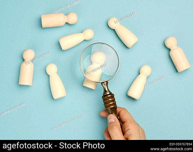 wooden men and a magnifying glass on a blue background. Recruitment concept, search for talented and capable employees, career growth, flat lay