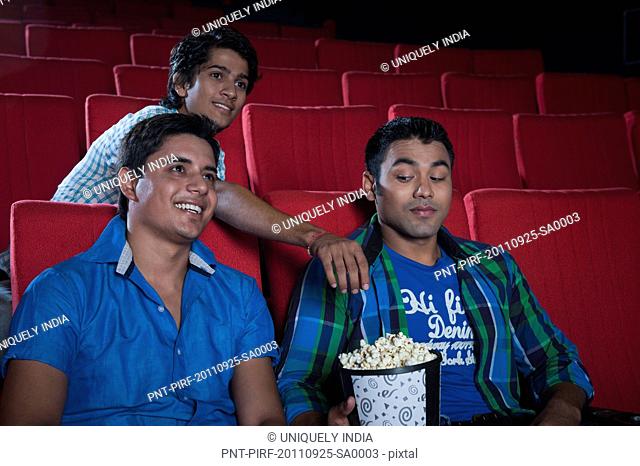 Man stealing popcorn from two friends enjoying movie in a cinema hall