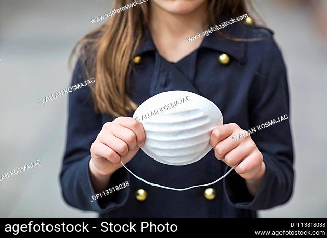 Young girl stands holding protective mask in her hands during the Coronavirus World Pandemic; Toronto, Ontario, Canada