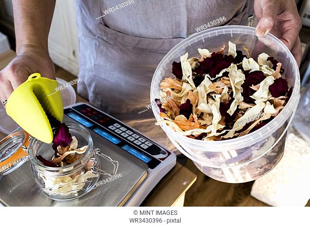 High angle close up of woman standing in a kitchen, weighing dried food on electronic kitchen scales