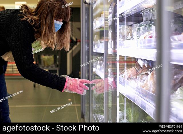 Woman wearing mask choosing vegetables in refrigerated section at supermarket