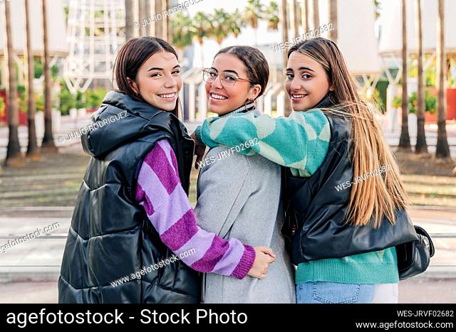 Smiling young women in warm clothing walking on footpath