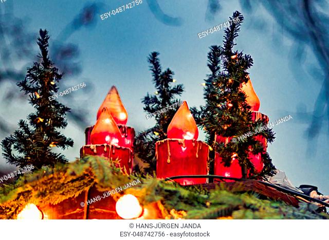 Big red plastic christmas candles are standing on a hut roof with fir branches and blue background