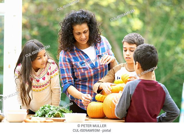 Mature mother and three children selecting homegrown pumpkins in kitchen