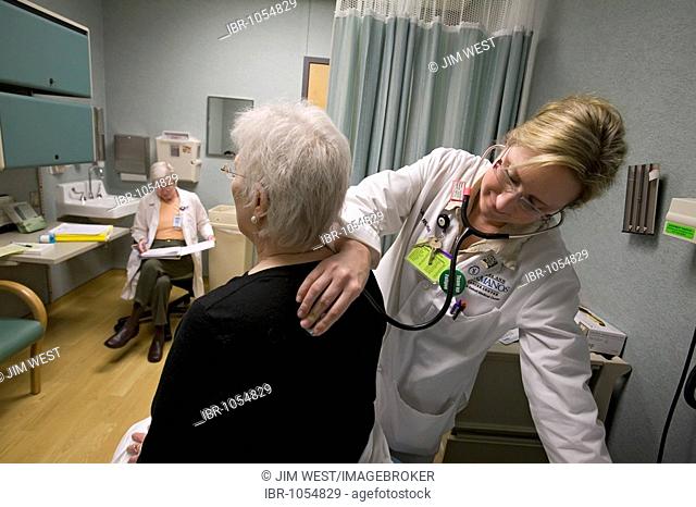 Nurse practitioner Sarah Jacob listens to Pat Lancaster's lungs with a stethoscope, as research nurse Susan Newell reviews her notes