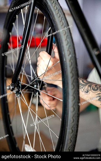 Close-up of young adult man reparigin bicycle wheel