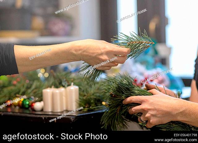 Woman's hand gives a pine twig to another woman who is handmade preparing Christmas decorations close up