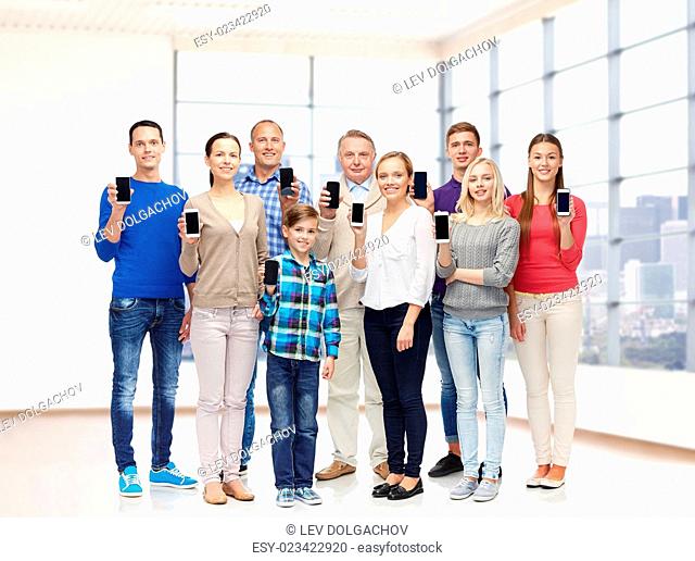 family, technology, generation and people concept - group of smiling men, women and boy with smartphones over empty office room or home