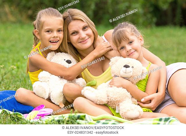 Two daughter kissing and hugging her mother lying on the grass on a picnic
