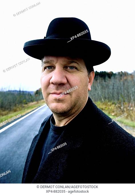 Portrait of a man in a black hat and overcoat standing on a country road