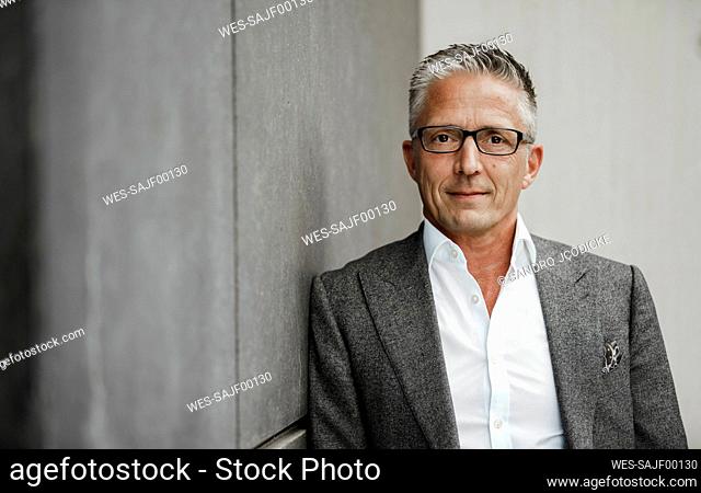 Businessman wearing eyeglasses leaning on gray wall