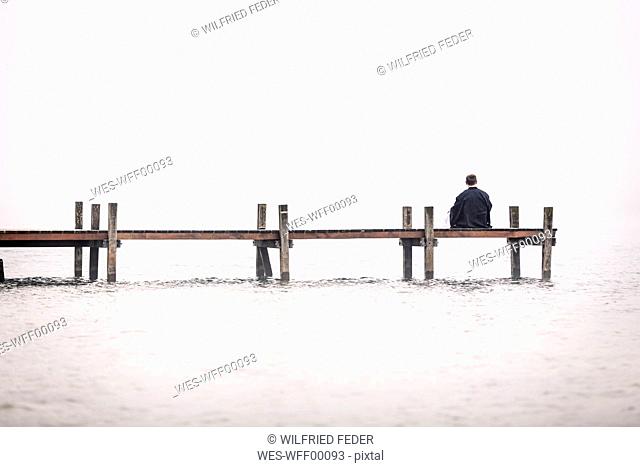 Back view of man sitting on jetty at Lake Starnberg, Germany