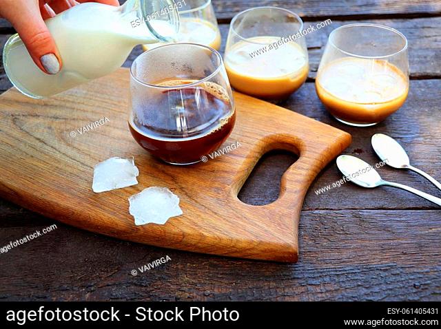 Women hand pouring iced milk sauce into coffee glass. Refreshing summer drink