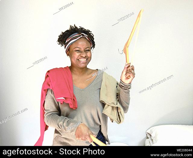 Portrait of young black woman with afro hairstyle with clothes on hangers indoor at home. Lifestyle concept