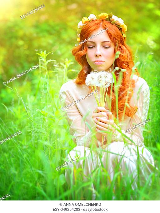 Portrait of a beautiful female wearing floral wreath on red curly hair, enjoying spring garden, holding in hands bouquet of dandelion flowers