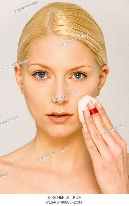 Young woman using cotton pad on face, portrait
