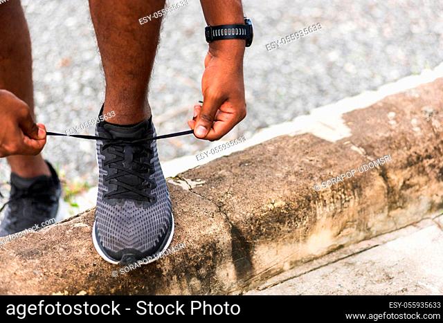 Close up Asian sport runner black man wear watch stand step on the footpath trying shoelace running shoes getting ready for jogging and run outdoor street...