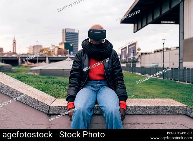 Italy, Woman withÊVRÊgoggles sitting on wall in city