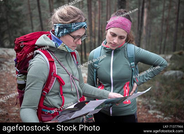 Two women read hiking map while hiking in the forest in Tiveden National Park in Sweden