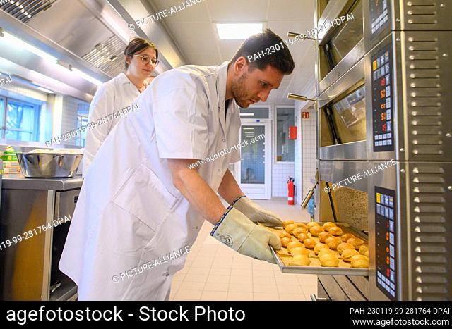 19 January 2023, Saxony-Anhalt, Bernburg: Ecotrophology students Timon-Joel Strauch (r) and Hannah Raudszus put a tray of legume bread rolls in the oven at...