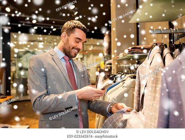 sale, shopping, fashion, technology and people concept - happy man or businessman in suit with smartphone choosing clothes at clothing store over snow