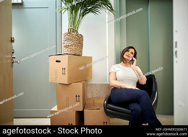 Mature woman sitting next to stack of boxes and using phone