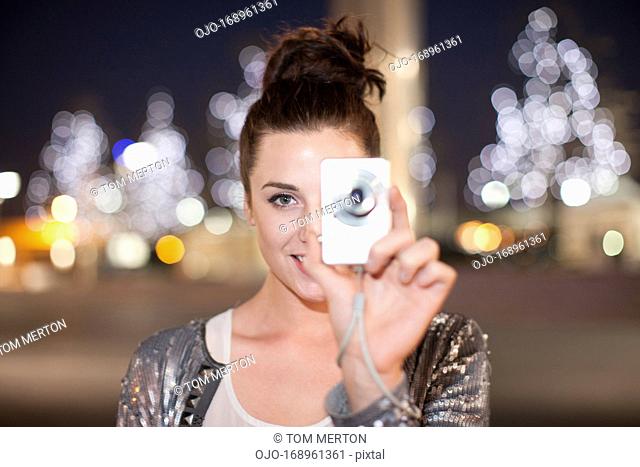 Woman taking picture on city street at night