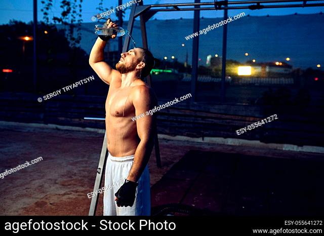 Tired muscular man doused with water, street workout. Fitness training on sports ground outdoor, male person pumps muscles, active urban lifestyle