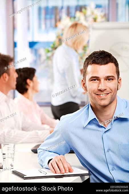 Happy young businessman in business meeting at office, looking at camera smiling