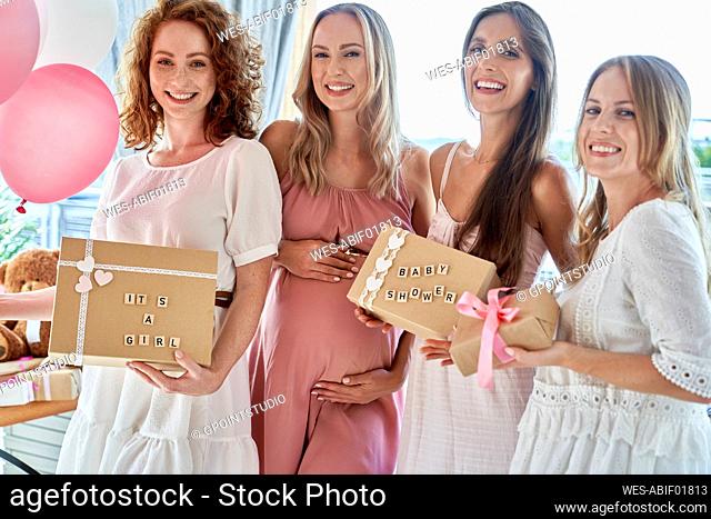 Smiling pregnant woman with friends holding gift boxes at baby shower