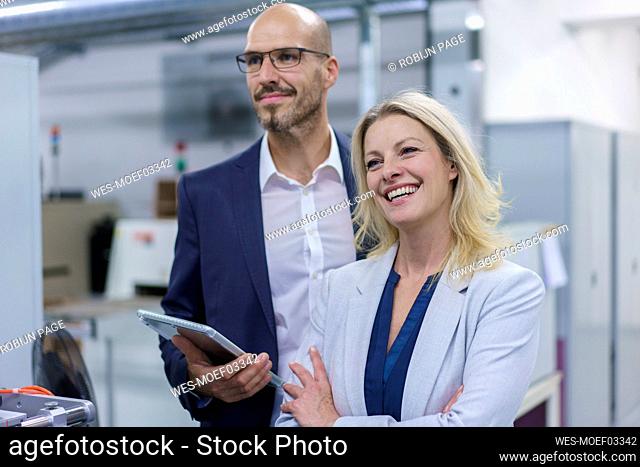 Cheerful businesswoman standing by colleague while looking away in factory