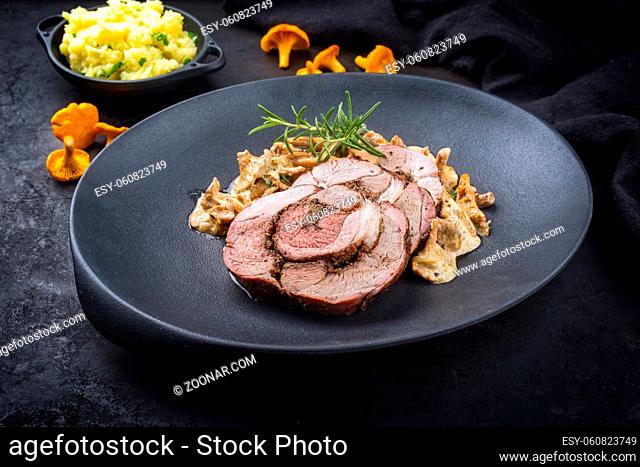 Traditional French barbecue lamb roast sliced with chanterelles in cream sauce and mashed potatoes offered as close-up on a design cast-iron plate