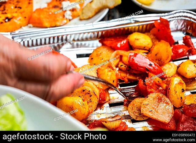 Grilled potatoes and tomatoes served on aluminium foil tray straight from grill, closeup detail