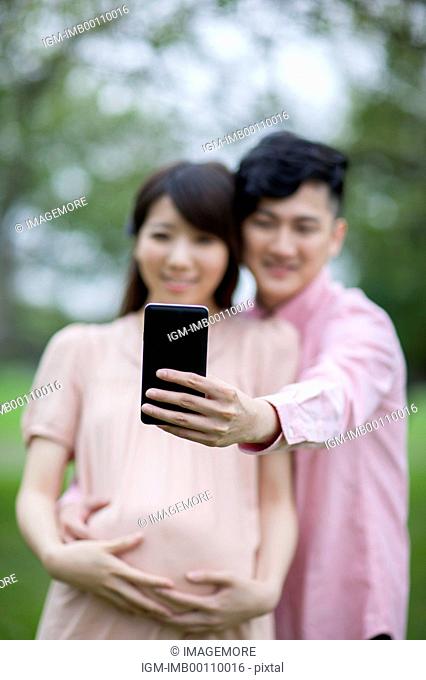 Young man and pregnant woman looking at the mobile phone and taking pictures with smile