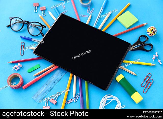 tablet pc and school supplies on blue background