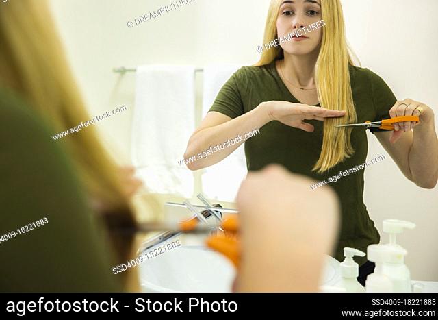 Young woman in home bathroom cutting her own hair with scissors