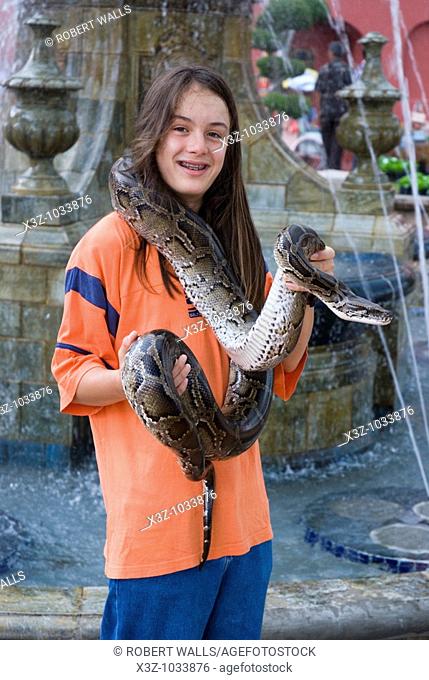 A long haired boy poses for s photo holding a python in Malacca Malaysia