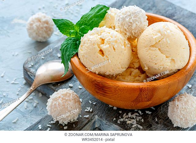 Balls of coconut ice cream with coconut flakes in a wooden bowl and green mint on the serving board