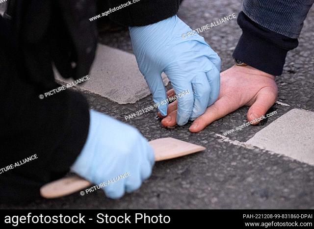 08 December 2022, Saxony, Dresden: A police officer removes a stuck hand of an environmental activist with olive oil from the roadway at a traffic light...