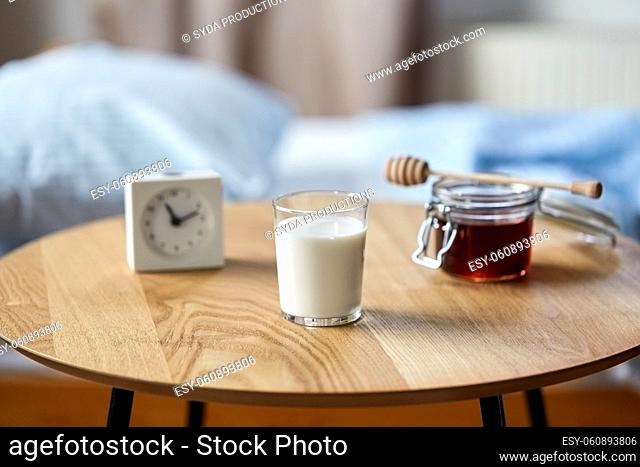 glass of milk, honey and alarm clock on table
