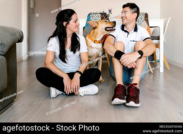 Smiling couple enjoying with dog while sitting on floor at home