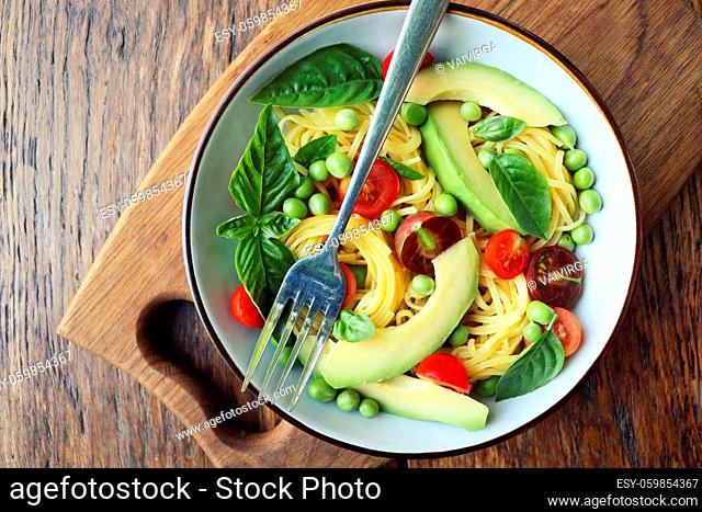 Pasta salad with green peas, avocado, cherry tomatoes and basil on rustic wooden background. Top view