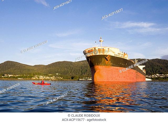 Caucasian man kayaking in front of big boat on skeena river at sunset in prince rupert northern british columbia canada