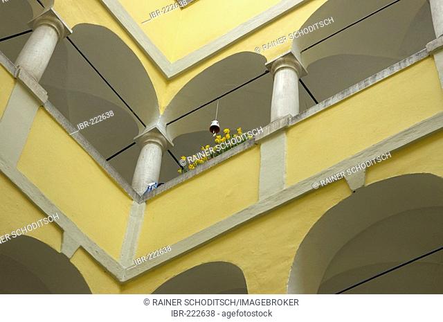 Detail of many historic arcades in a cour tyard with a yellow facade, a balcony, Graz, Austria