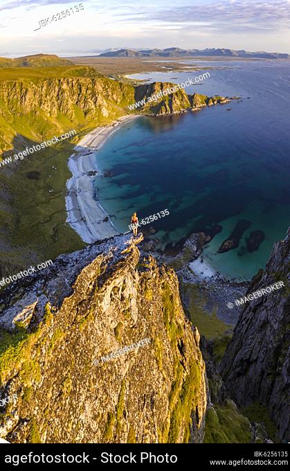 Evening atmosphere, hiker standing on a cliff, view to rocks, beach and sea, top of the mountain Måtinden, near Stave, Nordland, Norway, Europe