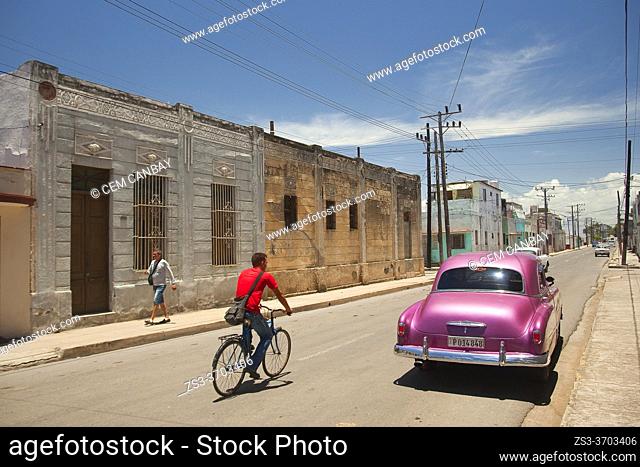 Cyclist and old American car in front of the colonial buildings at the historic center, Cienfuegos, Cienfuegos Province, Cuba, West Indies, Central America