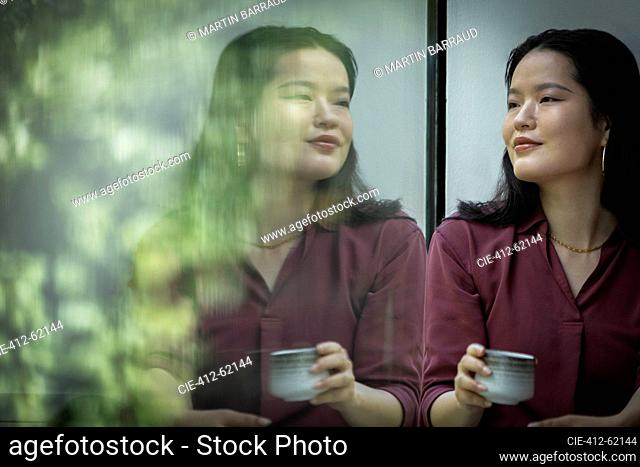 Thoughtful young woman drinking tea at window