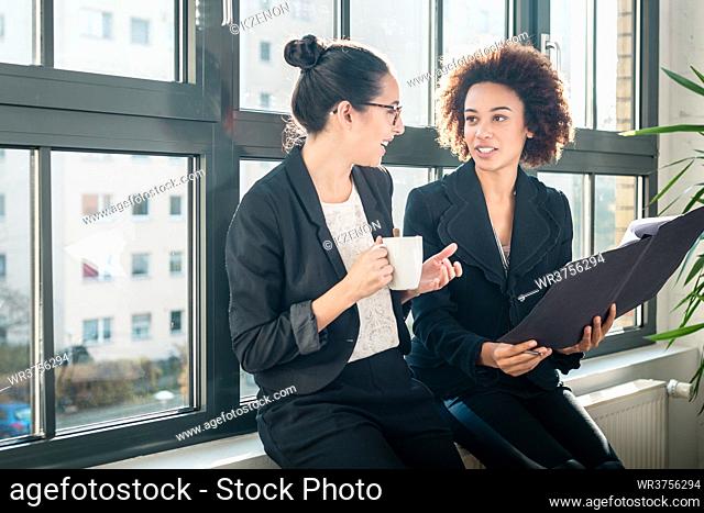 Two young female colleagues reviewing business reports during break in the office