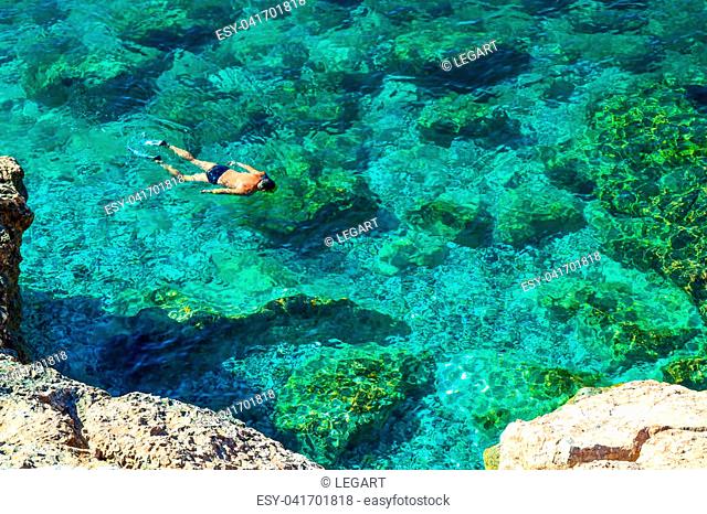 Nice view of the sea. Calm clear sea. At the bottom are large stones. The diver floats on the surface. View from above