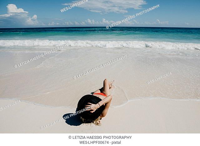 Mexico, Quintana Roo, Tulum, young woman with hat lying on the beach